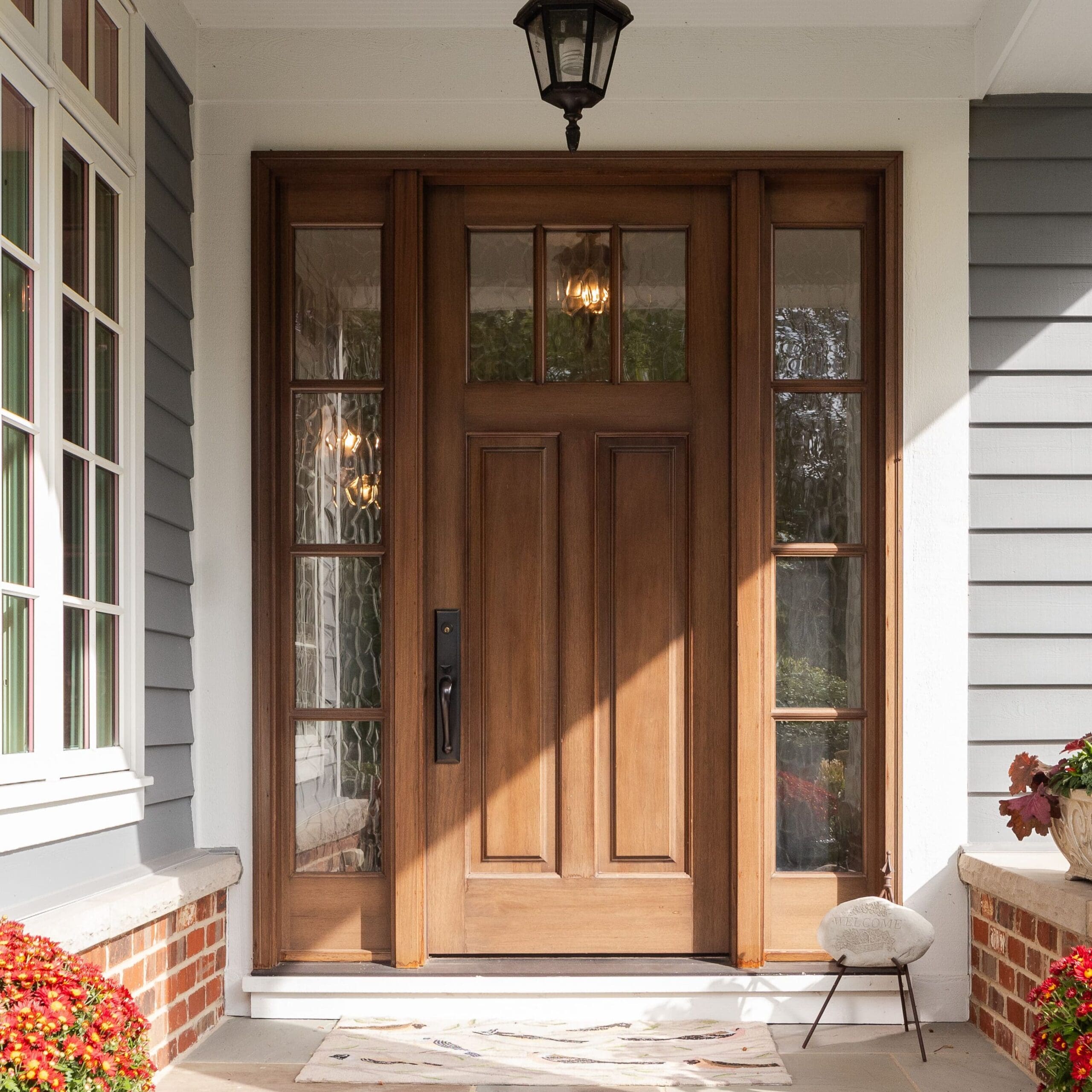 A front door and covered porch detail on a home with grey siding, white trim, red brick, a wooden front door.