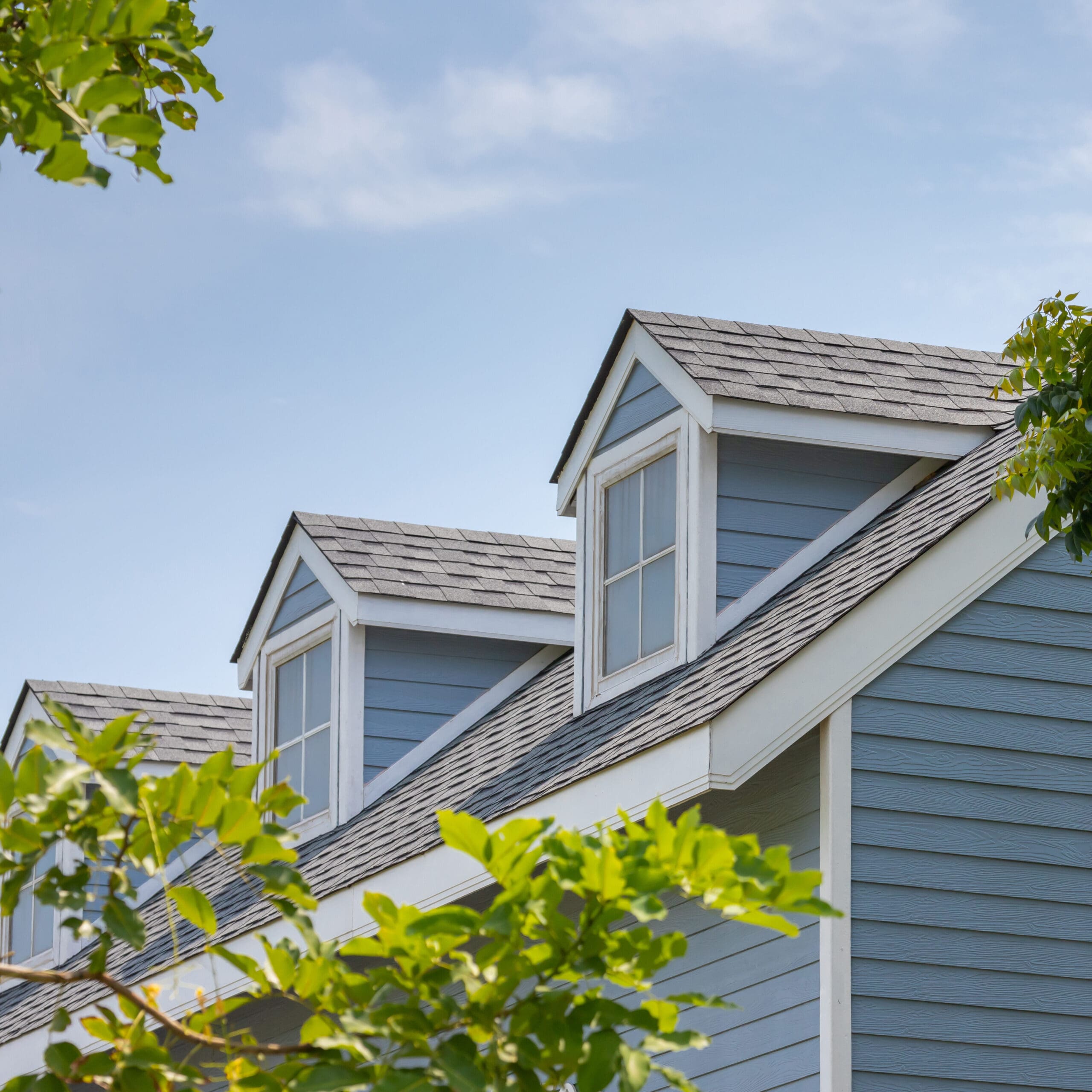 Roof shingles with garret house on top of the house among a lot of trees. dark asphalt tiles on the roof background