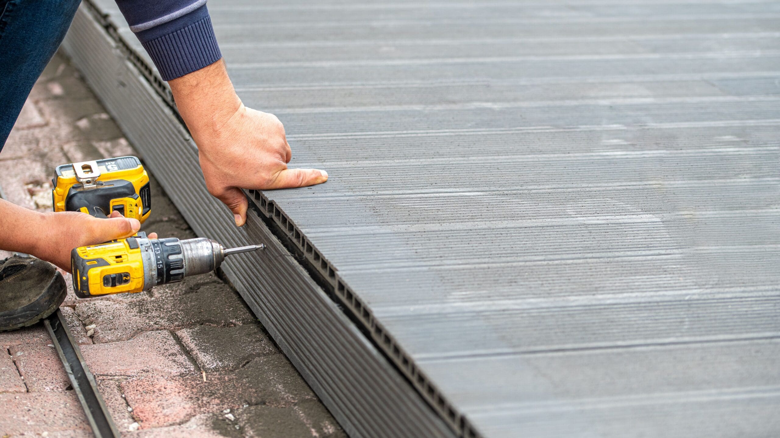 Man assembling composite deck using cordless screwdriver.